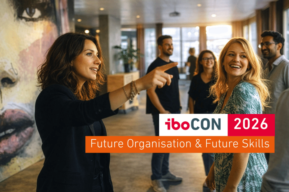 Leitmotiv der iboCON 2026 - Gruppe von Menschen in einem modernen Raum; eine Person zeigt erklärend nach vorne, eine andere lacht zur Gruppe. Zwei Gesichter im Vordergrund sind scharf, die übrigen Personen und die Architektur im Hintergrund leicht unscharf. Warmes Gegenlicht durch große Fenster erzeugt eine inspirierende, dynamische Aufbruchsstimmung.
