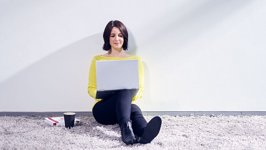 Flexible Weiterbildungen und Beratung durch ibo Frau sitzt mit einem Laptop an der Wand und besucht die ibo Website
